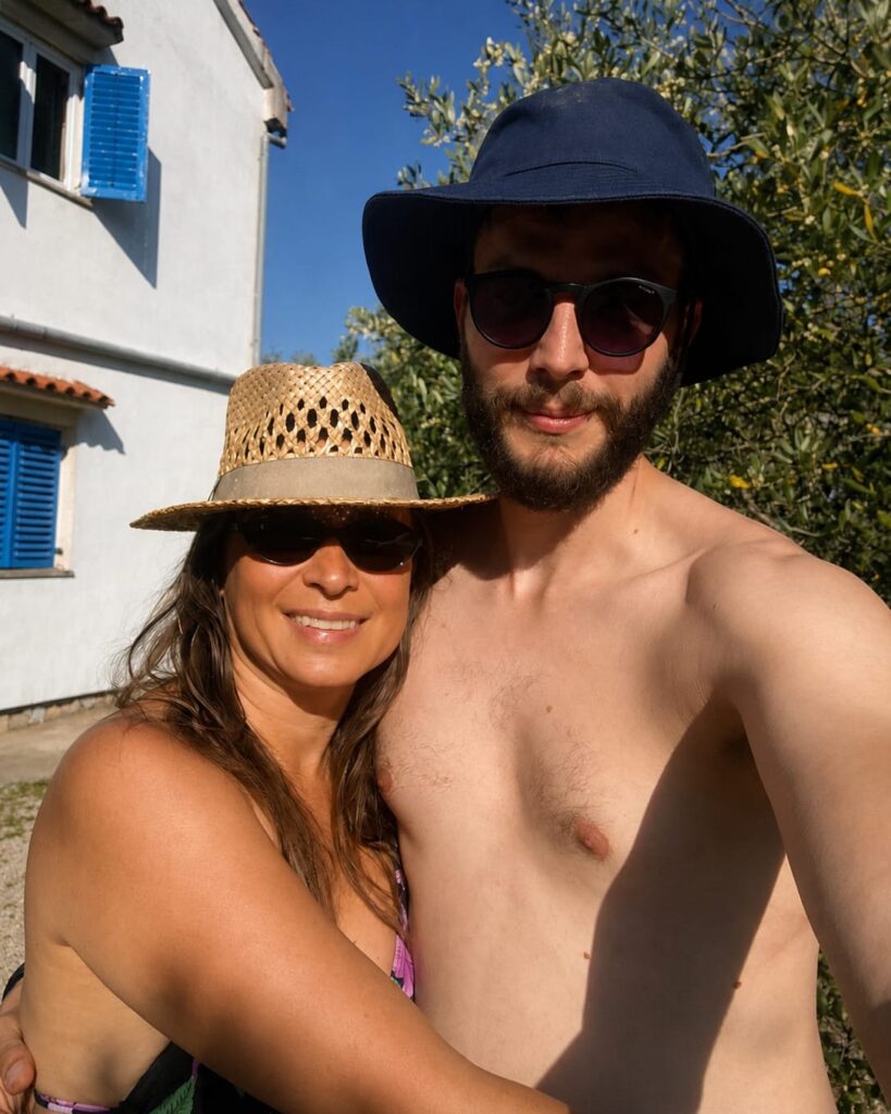 Couple embracing in front of a traditional house with blue shutters on Krk island during a summer renovation weekend.