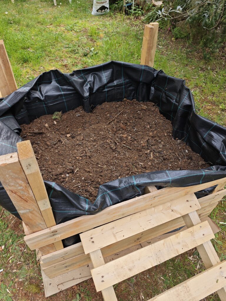 Adding compost to a DIY raised garden bed for sustainable vegetable gardening in Croatia