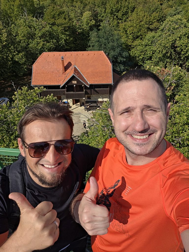 Za drugu fotografiju, gore u sredini:
Imam Alem Crnkić i još jedan sudionik nasmiješeni ispred planinarskog doma na Hrastovačkoj gori.